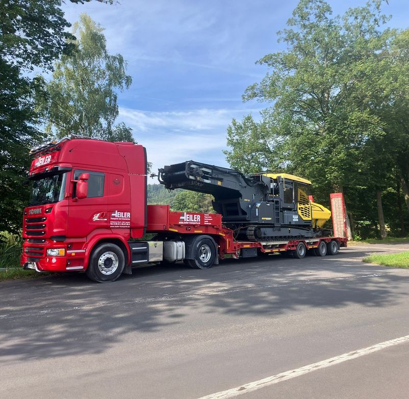 LKW fährt mit einem Bagger auf der Ladefläche auf der Straße